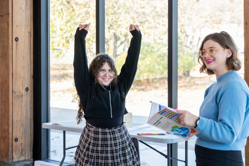 Une jeune avec les bras dans les airs, à côté de Margaret Fraser, codirectrice de Metalude.